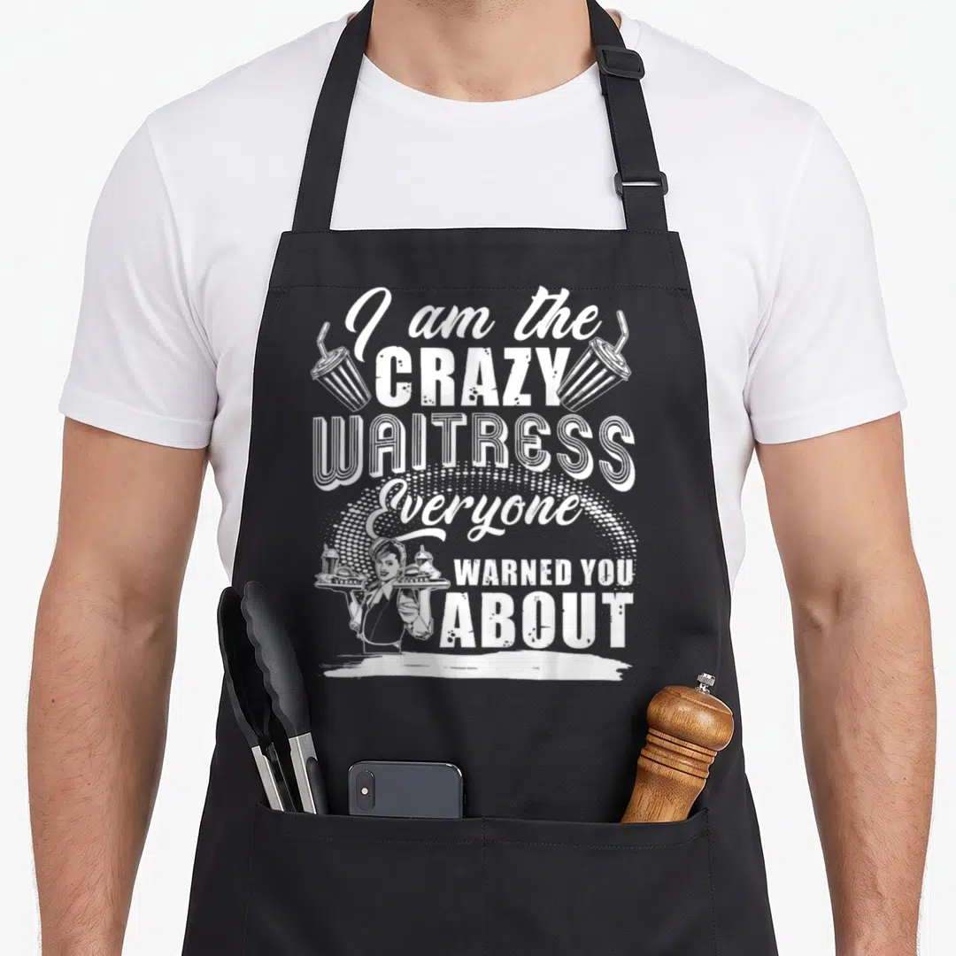 Waitress novelty apron - White stacked text reading I am the crazy waitress everyone warned you about with server — shown on a black cotton canvas apron against a white background