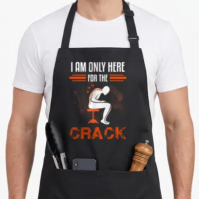 Chiropractic spine chiropractor apron - White silhouette on orange stool with text I AM ONLY HERE FOR THE CRACK — shown on a black cotton canvas apron against a white background