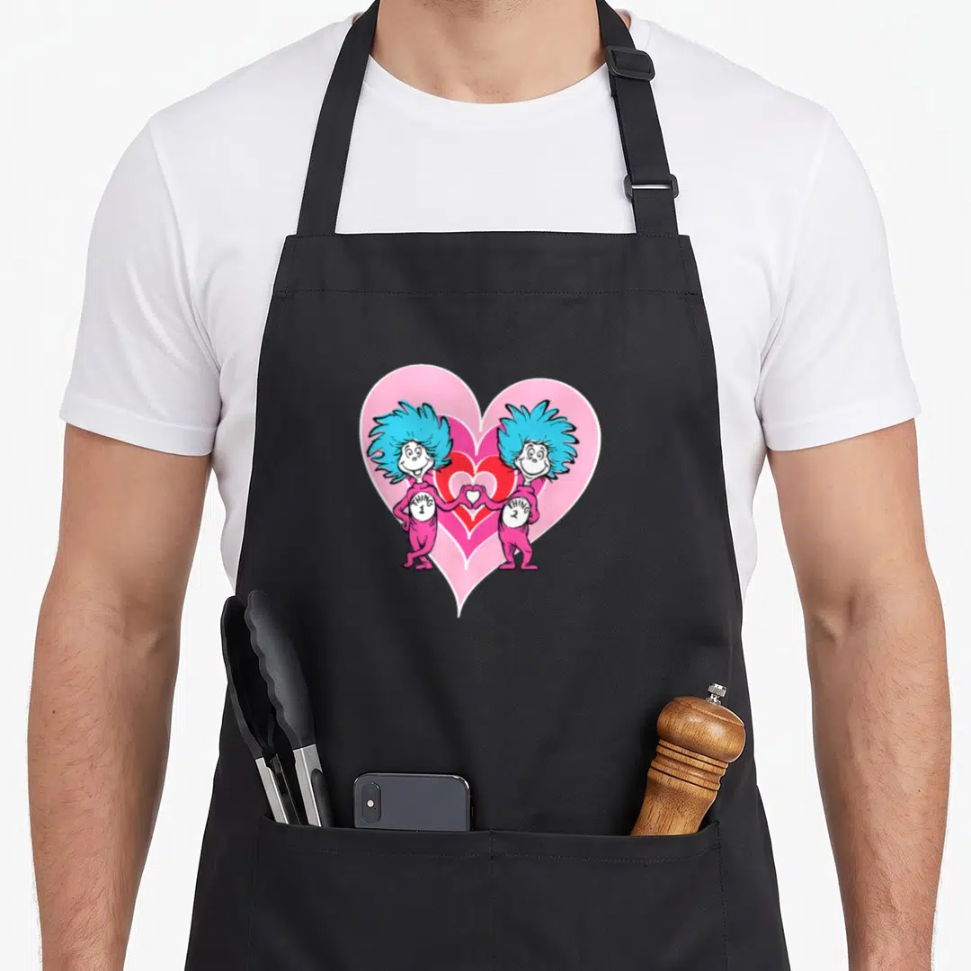 Retro general apron - Thing 1 and Thing 2 holding hands forming a heart inside a pink background — shown on a black cotton canvas apron against a white background