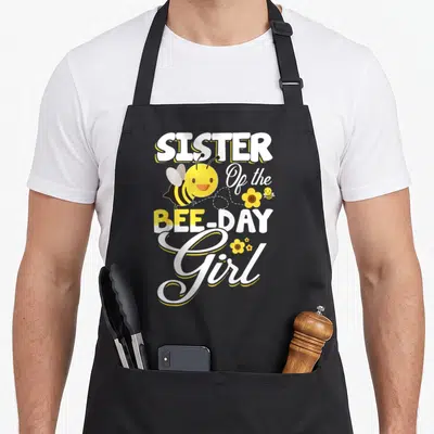 Sister bee aprons - Stacked SISTER Of the BEE-DAY Girl text with cartoon bees and yellow flowers — shown on a black cotton canvas apron against a white background