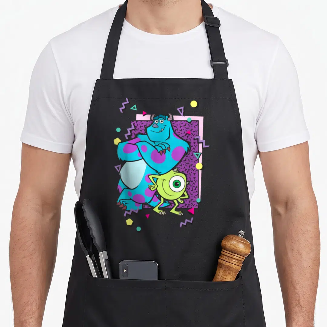 Mike 90s apron - Sulley and Mike centered on purple patterned rectangle with colorful geometric shapes and zigzags — shown on a black cotton canvas apron against a white background