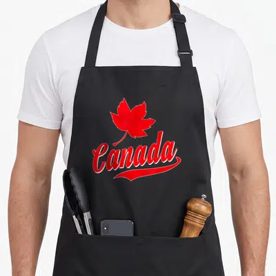 Leaf canada canadian aprons - Red maple leaf above red Canada script on black bib apron — shown on a black cotton canvas apron against a white background