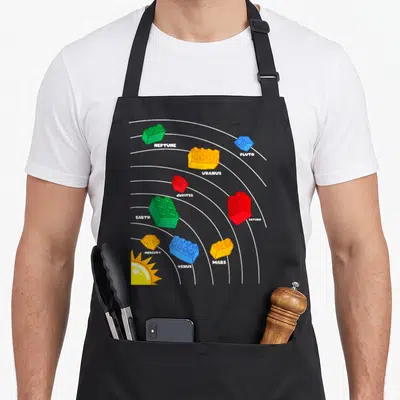 Planet block & apron - Cartoon solar system with colored plastic bricks labeled NEPTUNE, PLUTO, URANUS, JUPITER — shown on a black cotton canvas apron against a white background