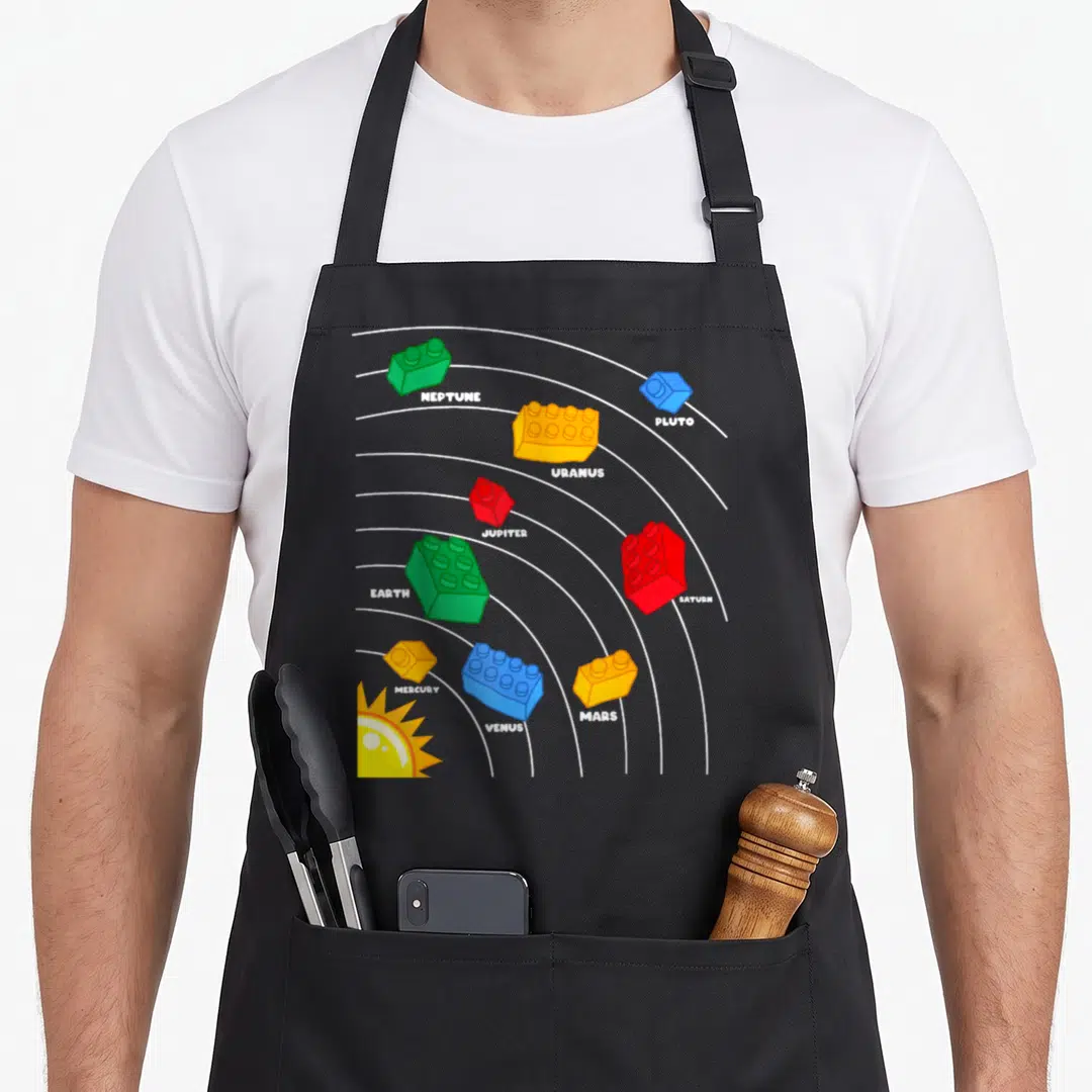Planet block & apron - Cartoon solar system with colored plastic bricks labeled NEPTUNE, PLUTO, URANUS, JUPITER — shown on a black cotton canvas apron against a white background