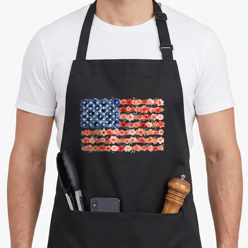 Floral 4th of july apron - Watercolor USA flag made of blue red and pink flowers with white stars — shown on a black cotton canvas apron against a white background