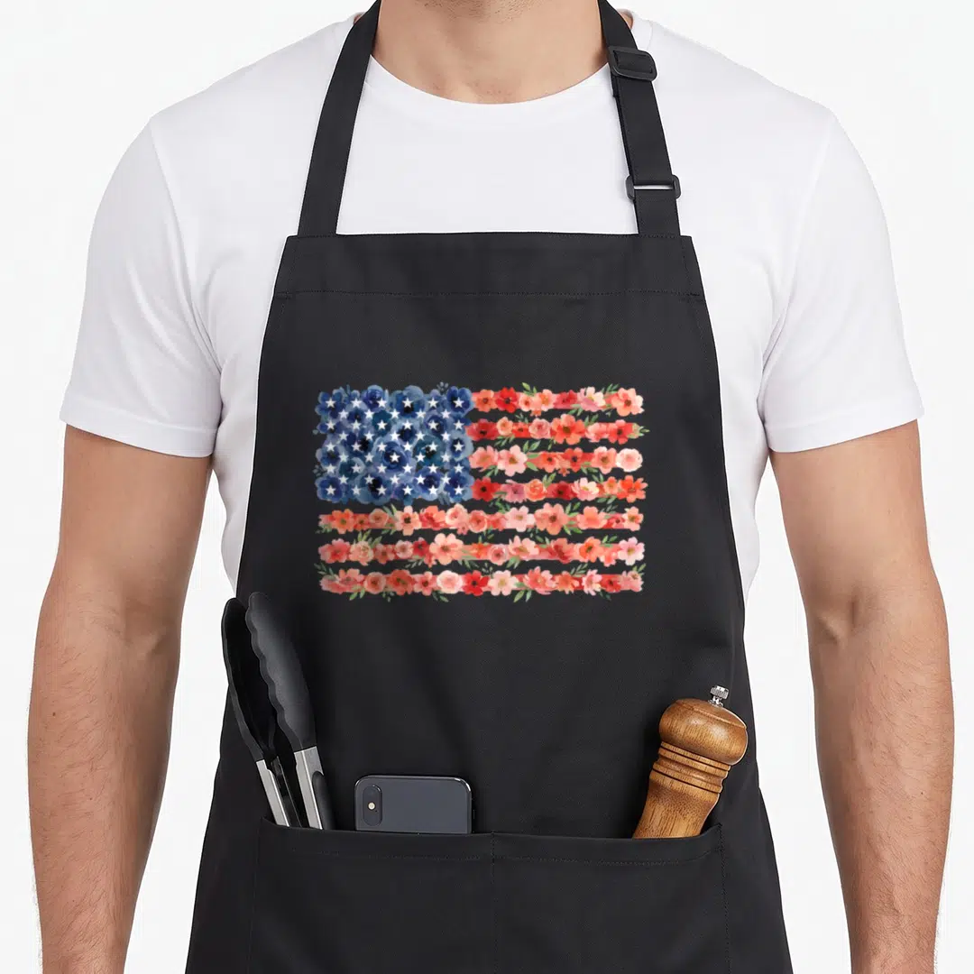 Floral 4th of july apron - Watercolor USA flag made of blue red and pink flowers with white stars — shown on a black cotton canvas apron against a white background
