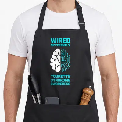 Brain salute apron - Cyan and white split brain graphic with WIRED DIFFERENTLY and Tourette Syndrome awareness text — shown on a black cotton canvas apron against a white background