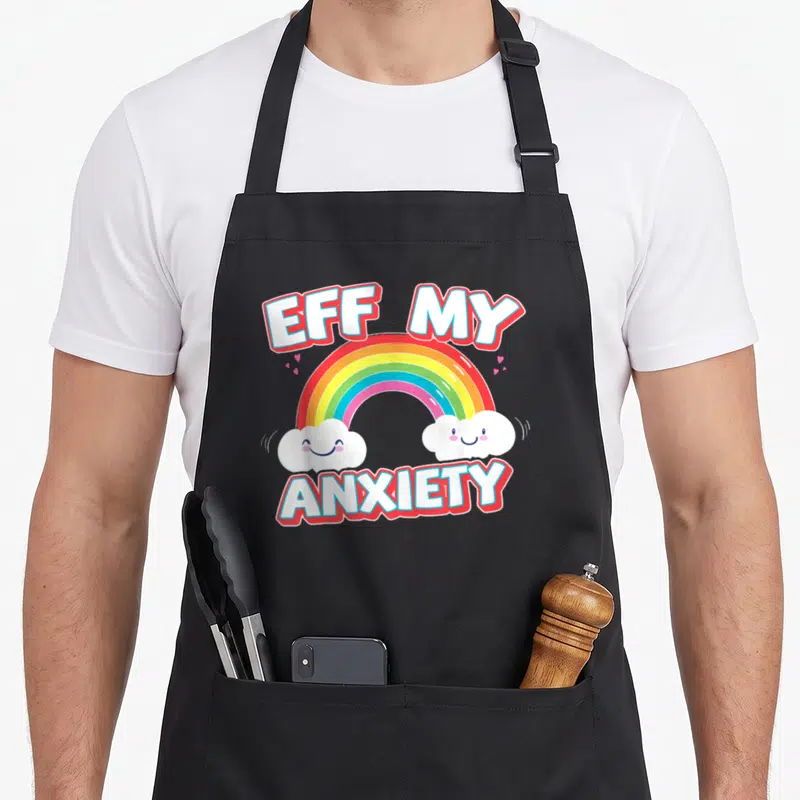 Eff anxiety apron - EFF MY ANXIETY text with rainbow, two smiling clouds, and pink hearts — shown on a black cotton canvas apron against a white background