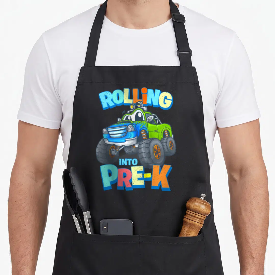 Clothe truck apron - Cartoon monster truck with Rolling Into Pre-K text in green blue and yellow — shown on a black cotton canvas apron against a white background