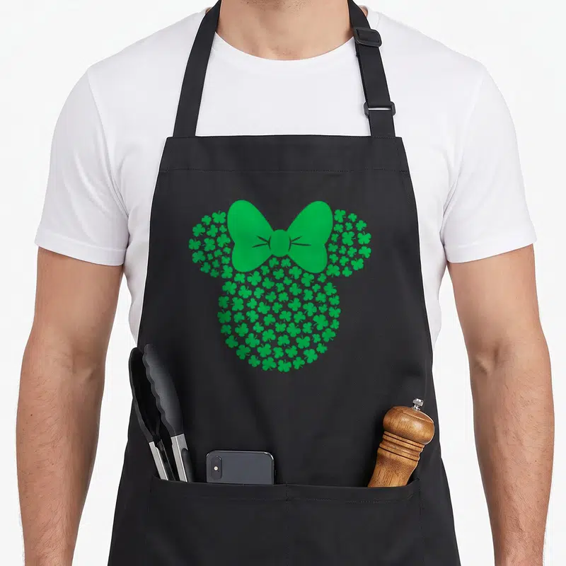 Leaf st patrick day aprons - Green silhouette of a head formed by clusters of shamrocks with a large bow on top — shown on a black cotton canvas apron against a white background