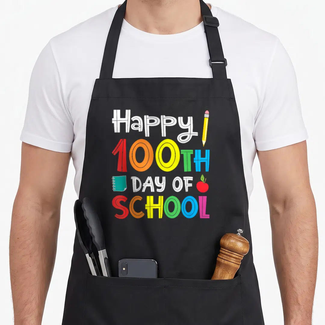 100th school teacher apron - Stacked text Happy 100TH DAY OF SCHOOL with pencil, notebook, and apple in red orange — shown on a black cotton canvas apron against a white background