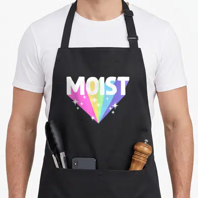 Moist meme apron - White MOIST text with five colored rays and white stars on black fabric — shown on a black cotton canvas apron against a white background