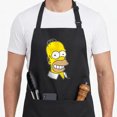 Homer face apron - Yellow cartoon head with white collar and wide grin — shown on a black cotton canvas apron against a white background