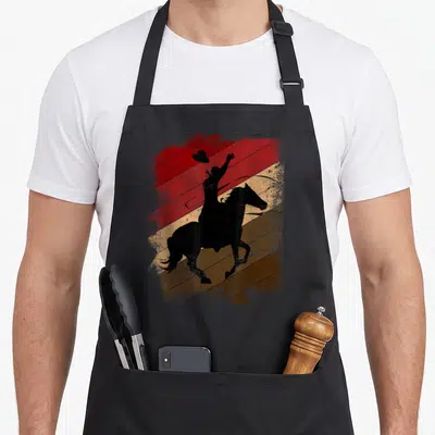 Rodeo farmer apron - Black cowboy silhouette tossing hat on bucking horse over red beige and brown distressed stripes — shown on a black cotton canvas apron against a white background