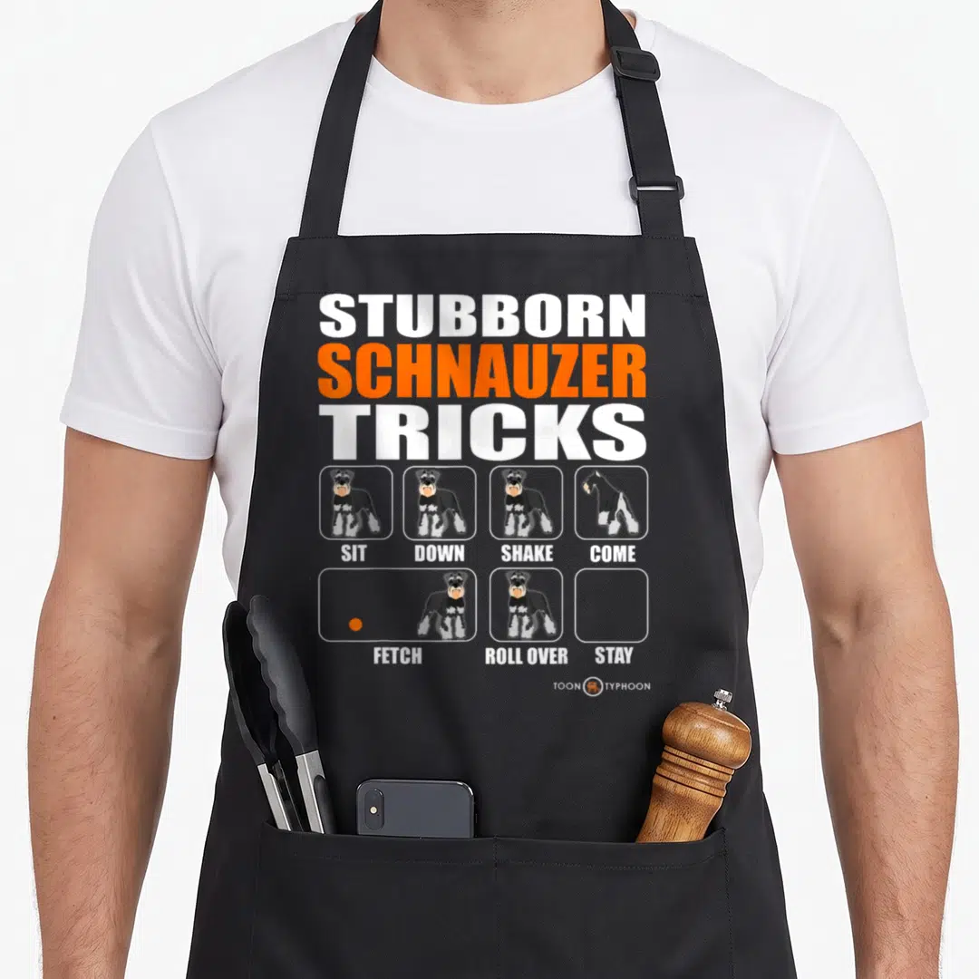 Stubborn schnauzer apron - Cartoon schnauzer grid with Sit Down Shake Come Fetch Roll Over Stay labels — shown on a black cotton canvas apron against a white background
