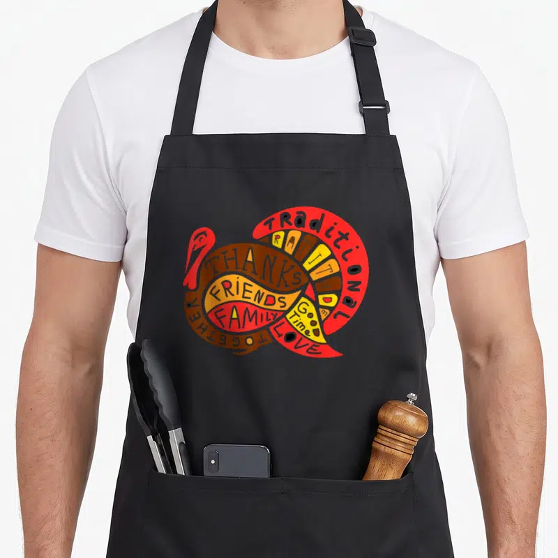Present thanksgiving day aprons - Cartoon turkey formed by red brown orange and yellow words including traditional — shown on a black cotton canvas apron against a white background