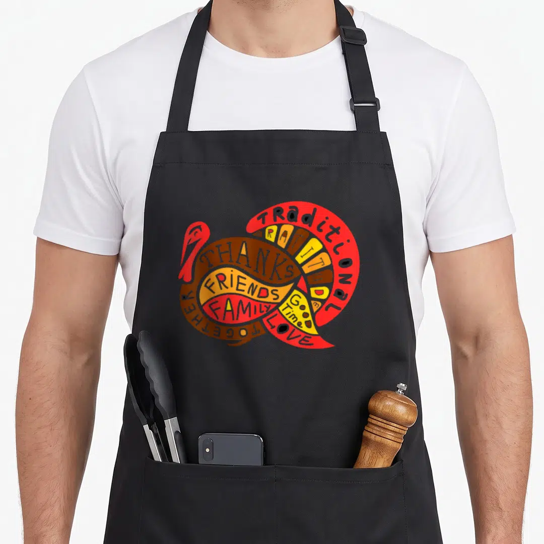 Present thanksgiving day aprons - Cartoon turkey formed by red brown orange and yellow words including traditional — shown on a black cotton canvas apron against a white background