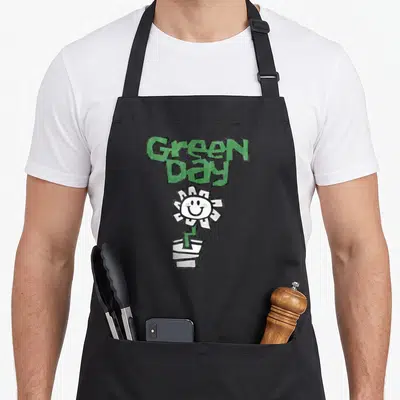 Flower plant apron - Stacked Green Day text above a white smiley flower in a striped pot — shown on a black cotton canvas apron against a white background