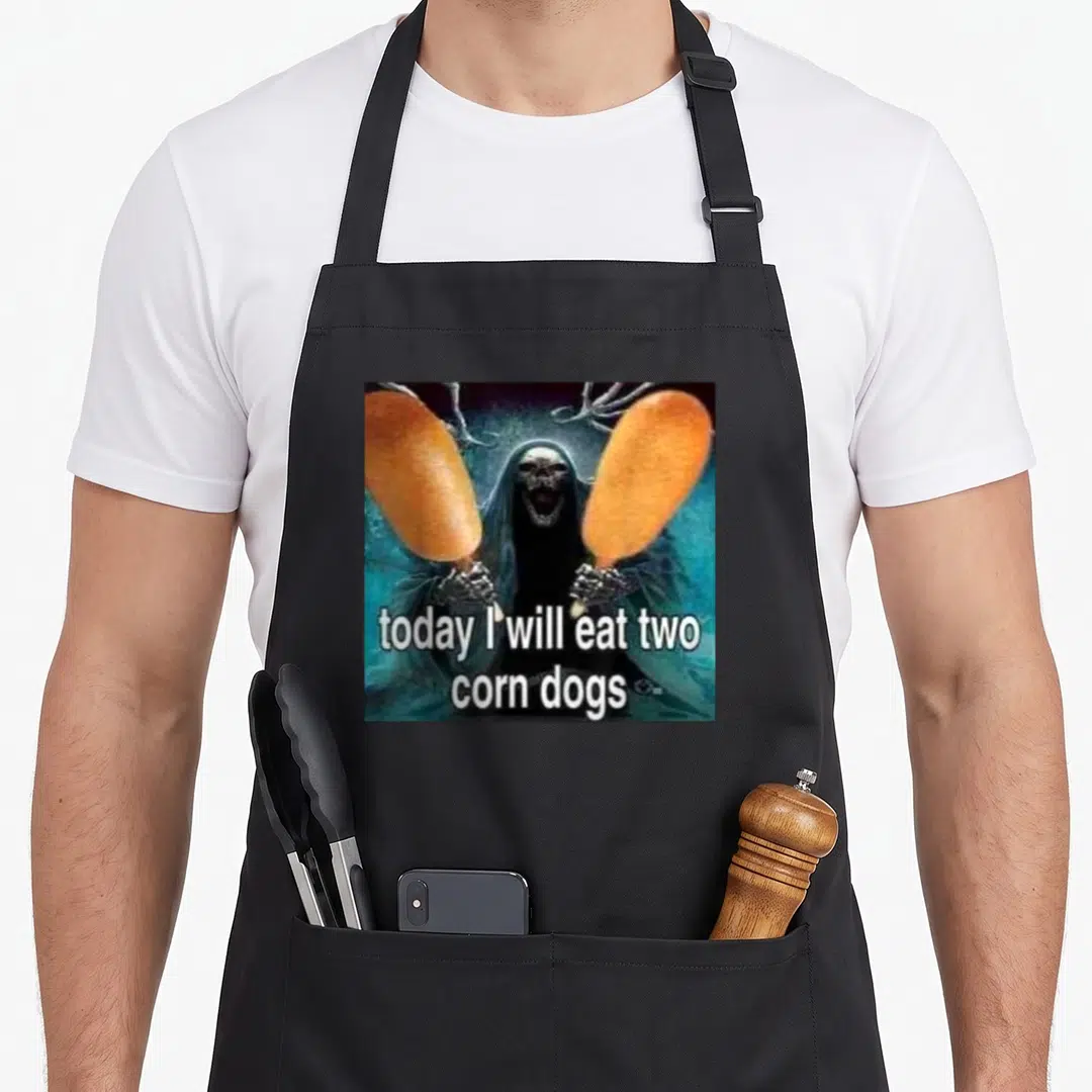 Eat dog apron - Grim reaper holding two orange corn dogs with white text overlay — shown on a black cotton canvas apron against a white background