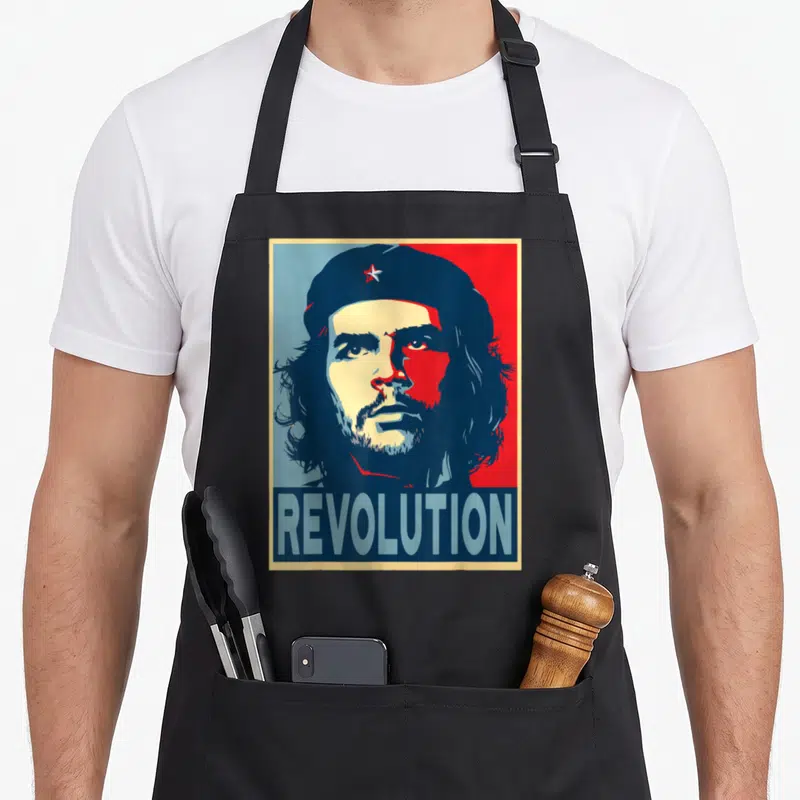 Che chevre apron - Retro Che Guevara portrait with REVOLUTION text in red blue cream — shown on a black cotton canvas apron against a white background