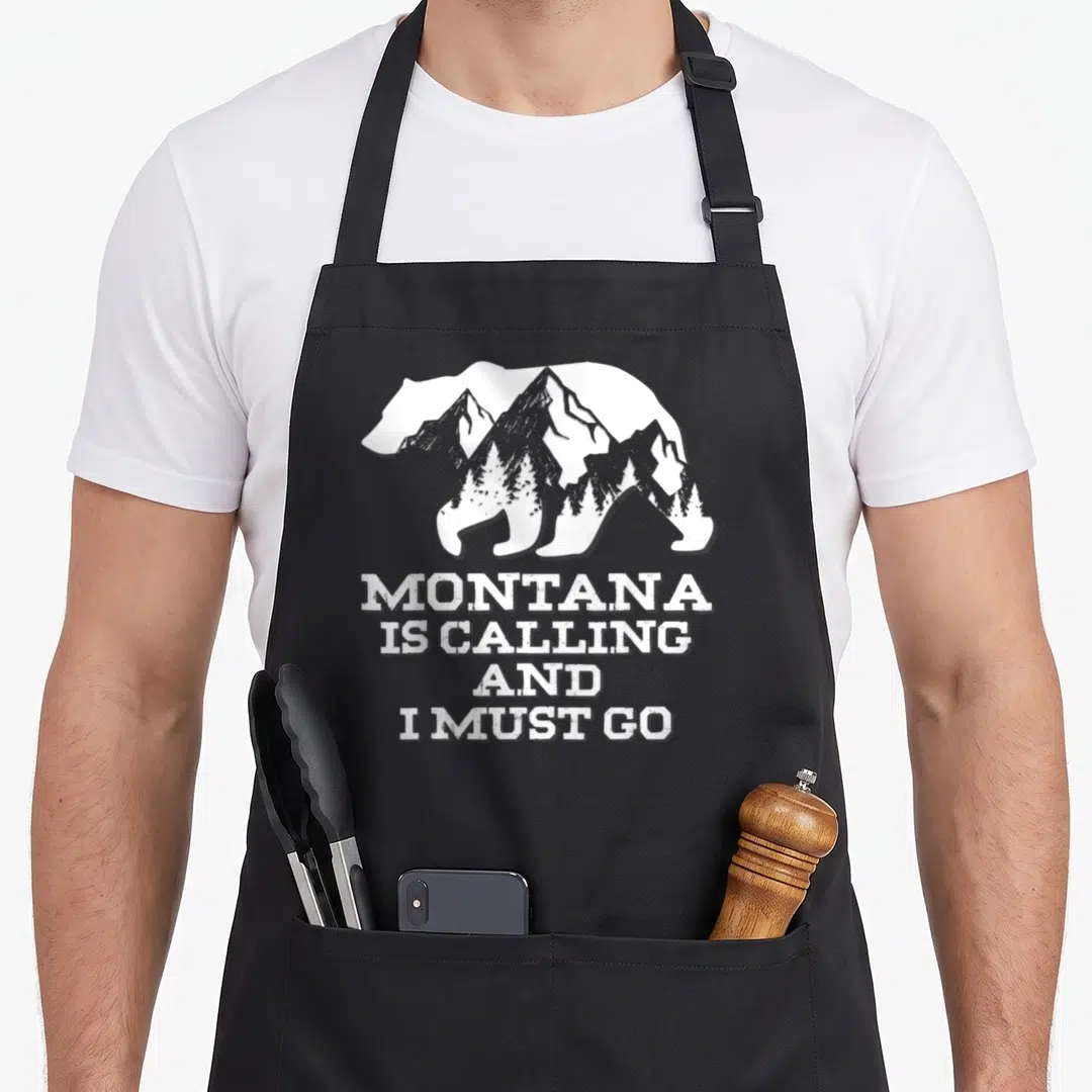 Must bear apron - White bear silhouette with mountains and pine trees above stacked distressed text — shown on a black cotton canvas apron against a white background