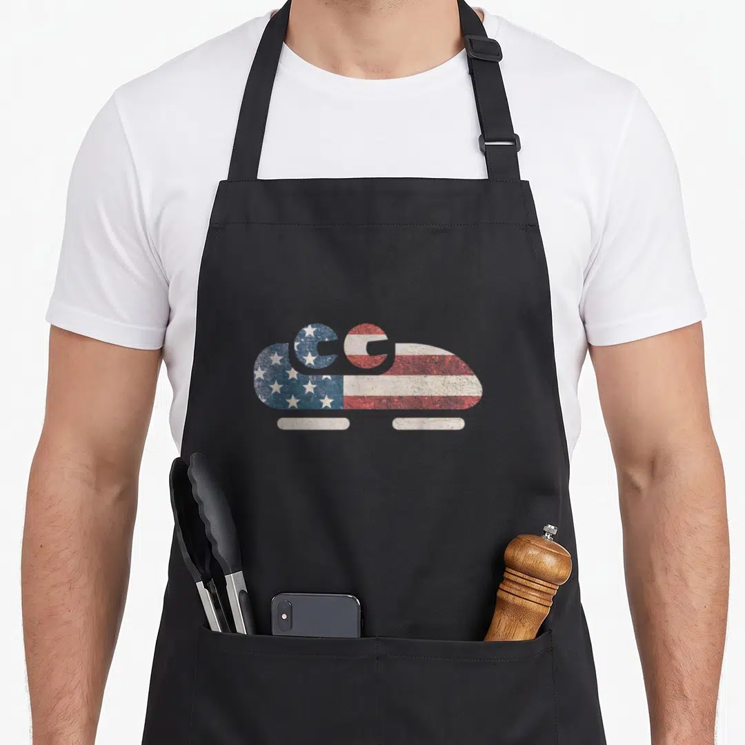 Bobsled american flag apron - Distressed camper van silhouette filled with blue stars and red white stripes — shown on a black cotton canvas apron against a white background