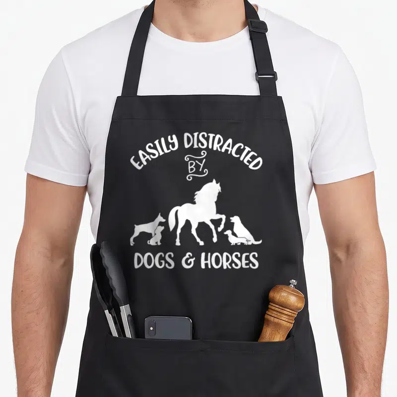 Easily dog apron - White EASILY DISTRACTED BY DOGS HORSES text with three dogs and one horse silhouette row — shown on a black cotton canvas apron against a white background