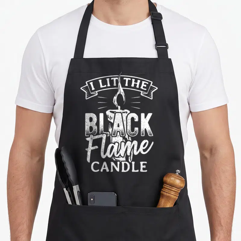 Lit spooky apron - White distressed candle graphic with I lit the black flame candle text arching over and stacking — shown on a black cotton canvas apron against a white background