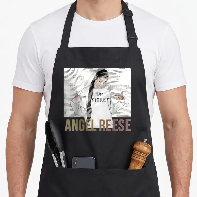 Reese angels in aprons - Woman pointing to The TICKET text with ANGEL REESE in gold below zebra stripes — shown on a black cotton canvas apron against a white background