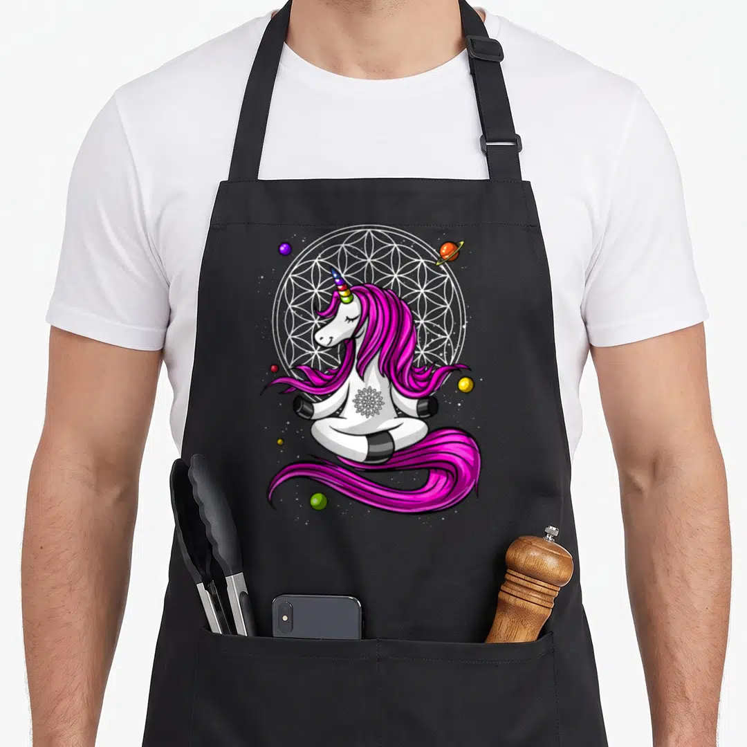 Zen unicorn apron - Cartoon unicorn meditating in lotus pose with pink mane and geometric circle background — shown on a black cotton canvas apron against a white background