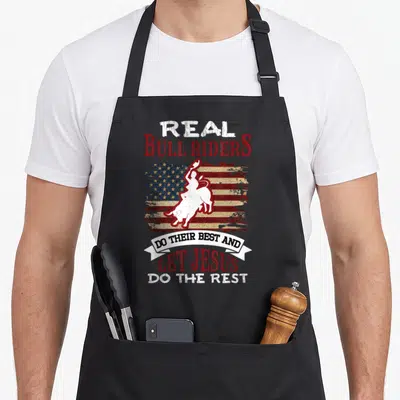 Bull christian apron - Red white blue distressed flag with white bull rider silhouette and stacked religious text — shown on a black cotton canvas apron against a white background