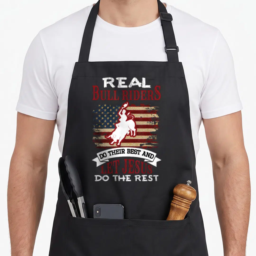 Bull christian apron - Red white blue distressed flag with white bull rider silhouette and stacked religious text — shown on a black cotton canvas apron against a white background