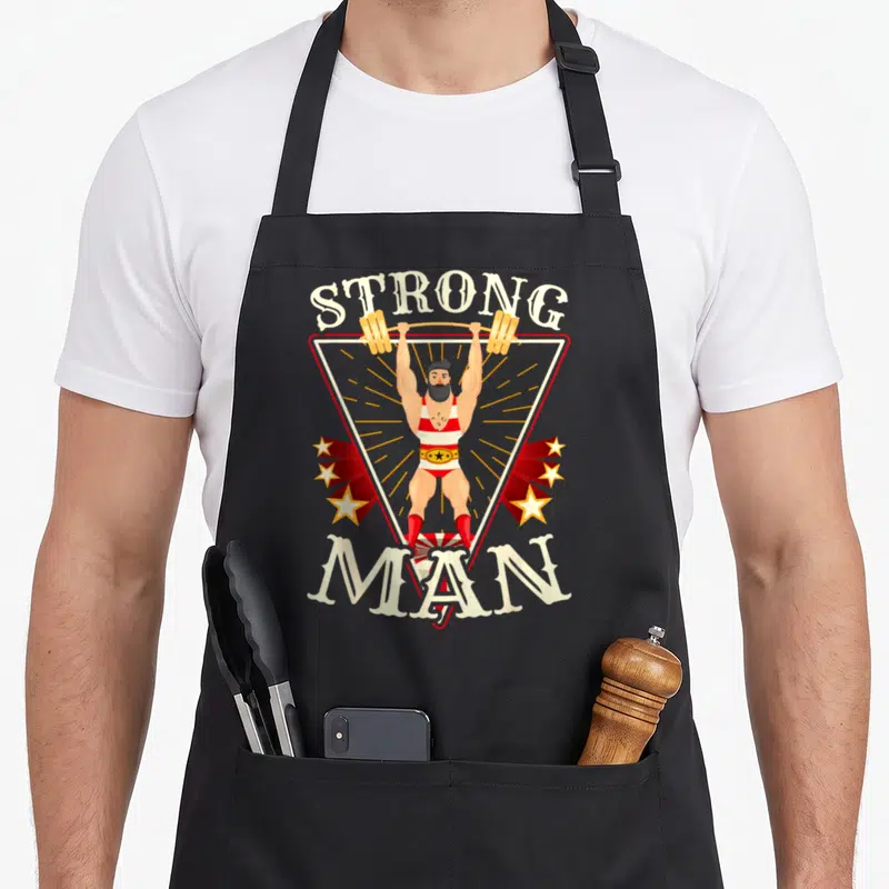 Strongman circus apron - Cartoon strongman lifting barbell in red white triangle with STRONG MAN text — shown on a black cotton canvas apron against a white background