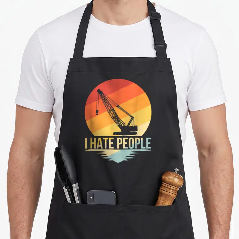 Hate construction apron - Retro crane silhouette against striped sun with I HATE PEOPLE text and water reflection — shown on a black cotton canvas apron against a white background