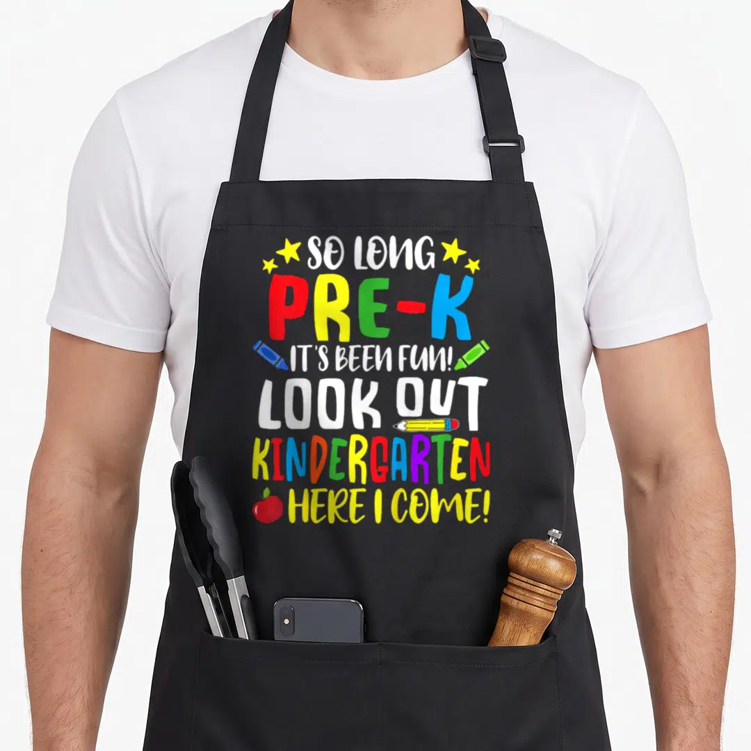 Kindergarten summer aprons - Stacked text So Long Pre-K Look Out Kindergarten with stars crayons pencil and apple — shown on a black cotton canvas apron against a white background