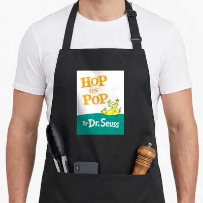 Book hop apron - Orange HOP ON POP text above yellow creatures lying and standing on teal background with By Dr. Seuss — shown on a black cotton canvas apron against a white background