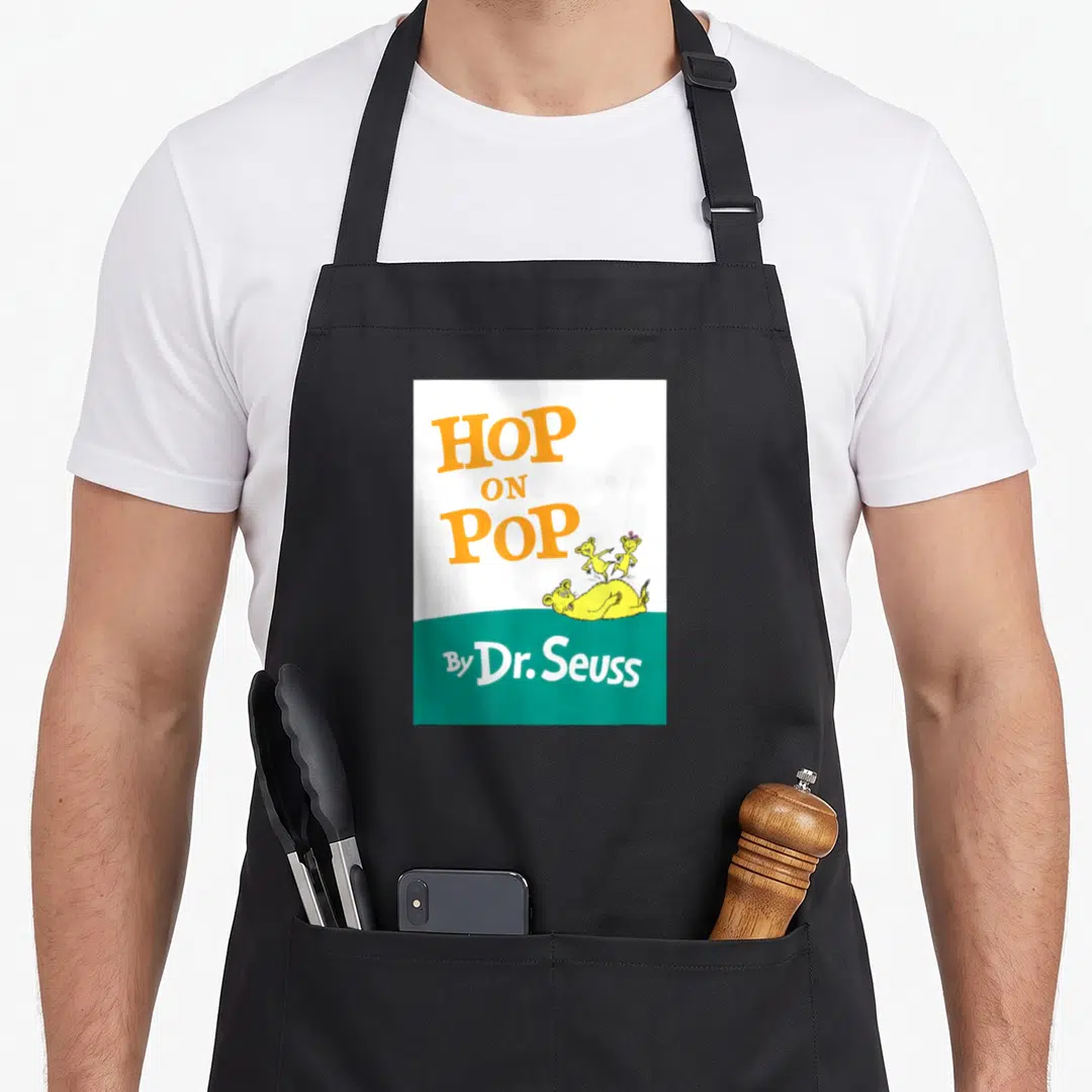 Book hop apron - Orange HOP ON POP text above yellow creatures lying and standing on teal background with By Dr. Seuss — shown on a black cotton canvas apron against a white background