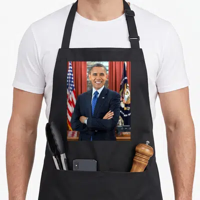 Barack patriotic apron - Photo portrait of man in navy suit with crossed arms between two flags — shown on a black cotton canvas apron against a white background