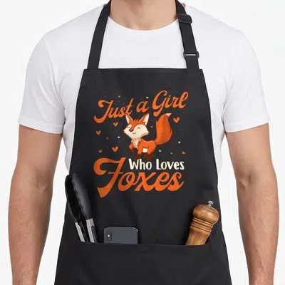 Zookeeper fox aprons - Cartoon fox illustration with orange script text and scattered hearts — shown on a black cotton canvas apron against a white background