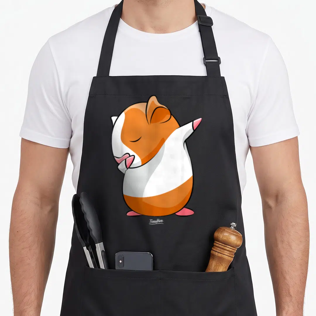 Dabbing pig dad apron - Cartoon guinea pig dabbing in orange, white, and pink colors — shown on a black cotton canvas apron against a white background