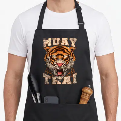 Asia thai girl apron - Distressed tiger head between MUAY and THAI text in orange and black — shown on a black cotton canvas apron against a white background