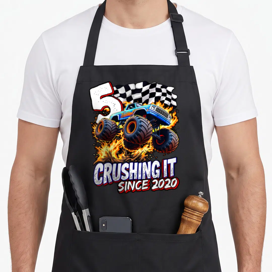 Monster 5th truck apron - Blue monster truck jumping through fire next to large number 5 and checkered flag — shown on a black cotton canvas apron against a white background