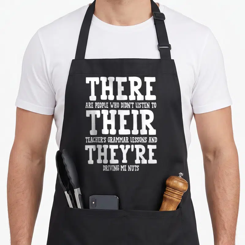 Appreciation christmas apron - White stacked typography quoting sarcasm about grammar lessons and driving nuts — shown on a black cotton canvas apron against a white background
