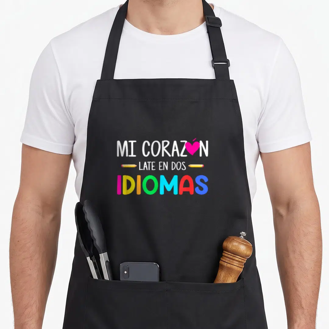 Corazon spanish aprons - MI CORAZON LATE EN DOS IDIOMAS text with pink heart and yellow pencils — shown on a black cotton canvas apron against a white background