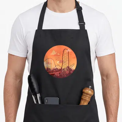 Artofclaire cedar apron - Circular orange and red minimalist illustration of a tall roller coaster tower and trees — shown on a black cotton canvas apron against a white background