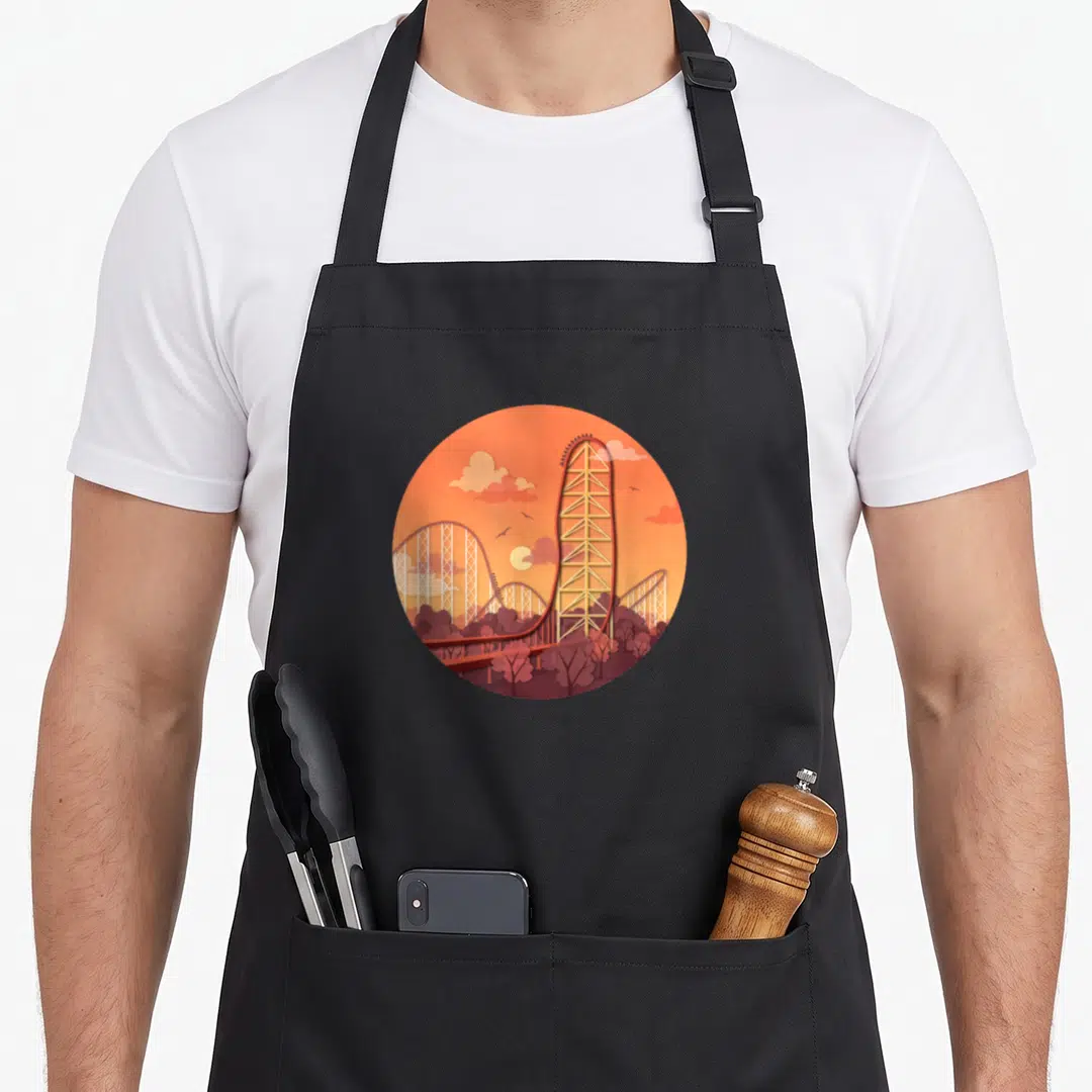 Artofclaire cedar apron - Circular orange and red minimalist illustration of a tall roller coaster tower and trees — shown on a black cotton canvas apron against a white background