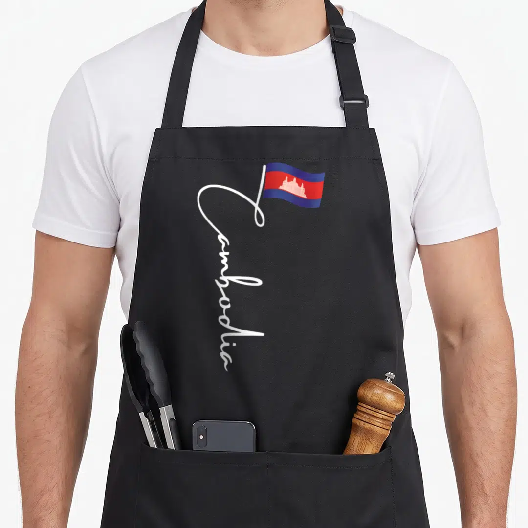 Wat cambodian apron - Vertical white Cambodia script with a waving blue and red flag attached to the letter — shown on a black cotton canvas apron against a white background
