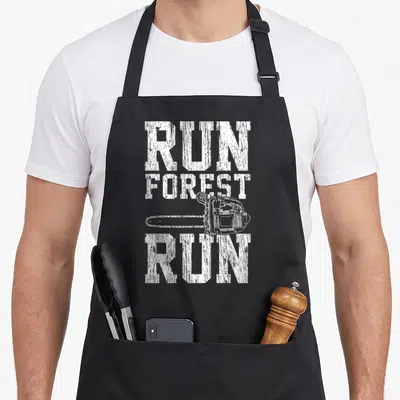 Run chainsaw apron - White distressed RUN FOREST RUN text with horizontal chainsaw illustration — shown on a black cotton canvas apron against a white background