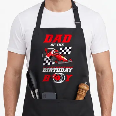 Race family car apron - DAD OF THE BIRTHDAY BOY text with red race car and tire replacing O in BOY — shown on a black cotton canvas apron against a white background