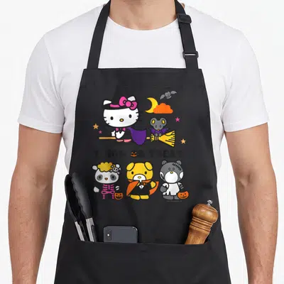 Cute friend halloween apron - Hello Kitty on broom with Trick or Treat text and three costumed animal friends below — shown on a black cotton canvas apron against a white background